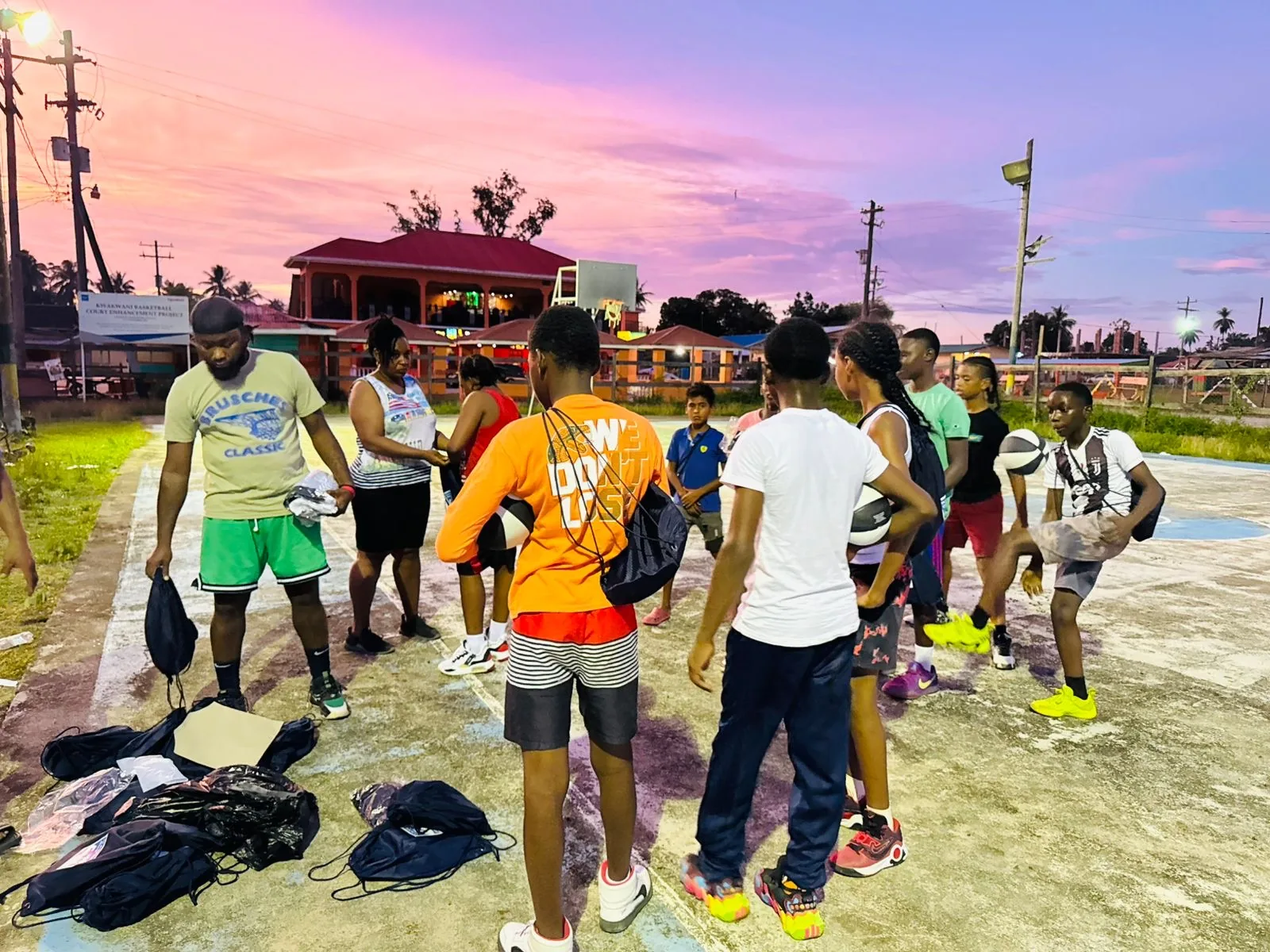 Young people gather around donated sports gear on a Kawkani basketball court