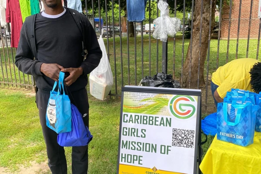 A recipient holds a blue care bag beside the Caribbean Girls Mission of Hope sign