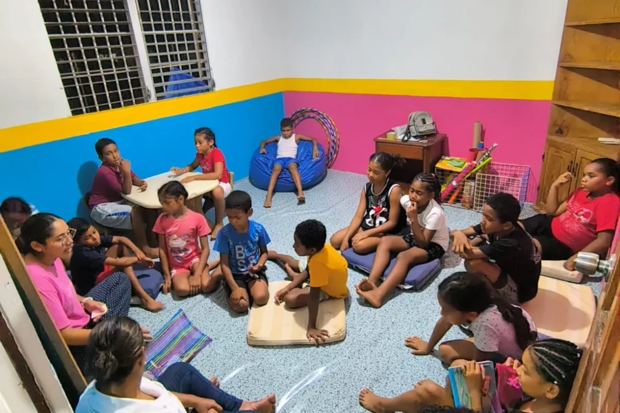 Children sit in a circle with volunteers inside the renovated community room