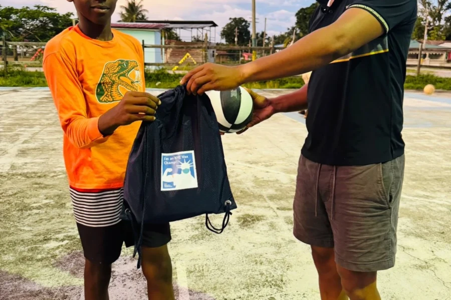 A young person receives a volleyball and drawstring bag from a volunteer